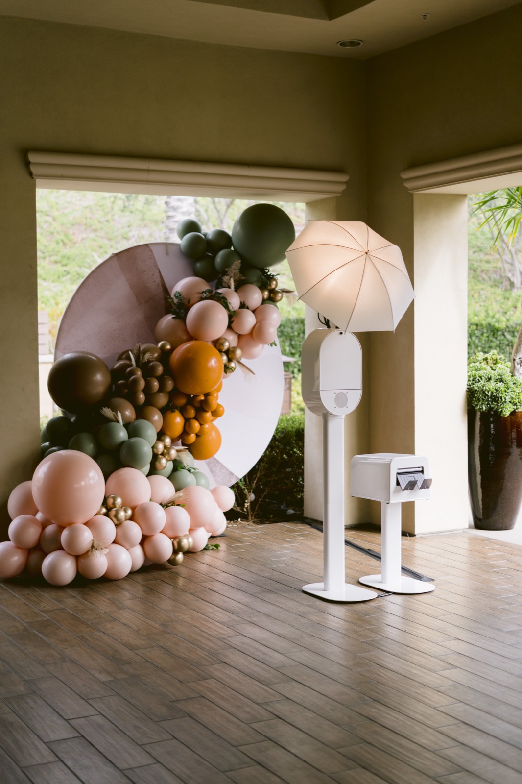 The white open-air booth and printer stand set up beside a blush, sage and orange balloon arch