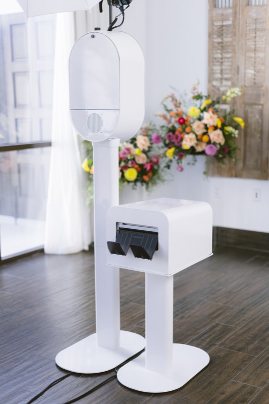 The white booth and printer stand in front of a bright floral arrangement